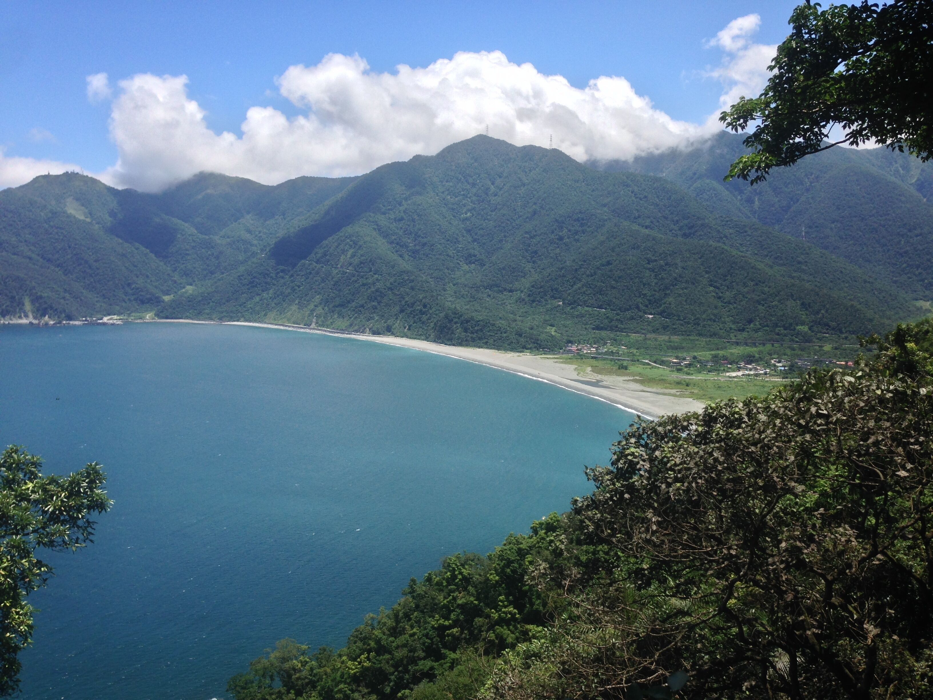 A coastal landscape with a beach, mountains, and a clear sky.