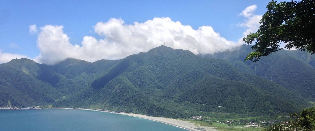 A coastal landscape with a beach, mountains, and a clear sky.