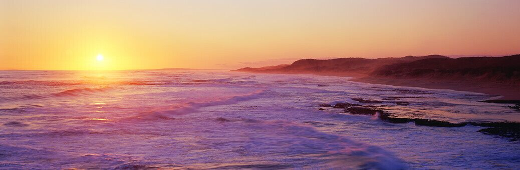 A sunset over a beach with waves and a distant shoreline.