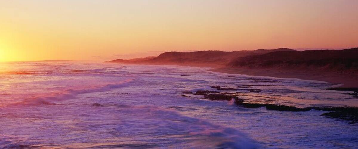 A sunset over a beach with waves and a distant shoreline.