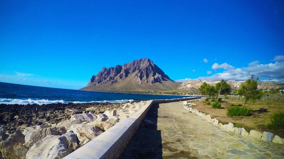 A coastal pathway leading to a rocky shoreline with a prominent mountain in the background.