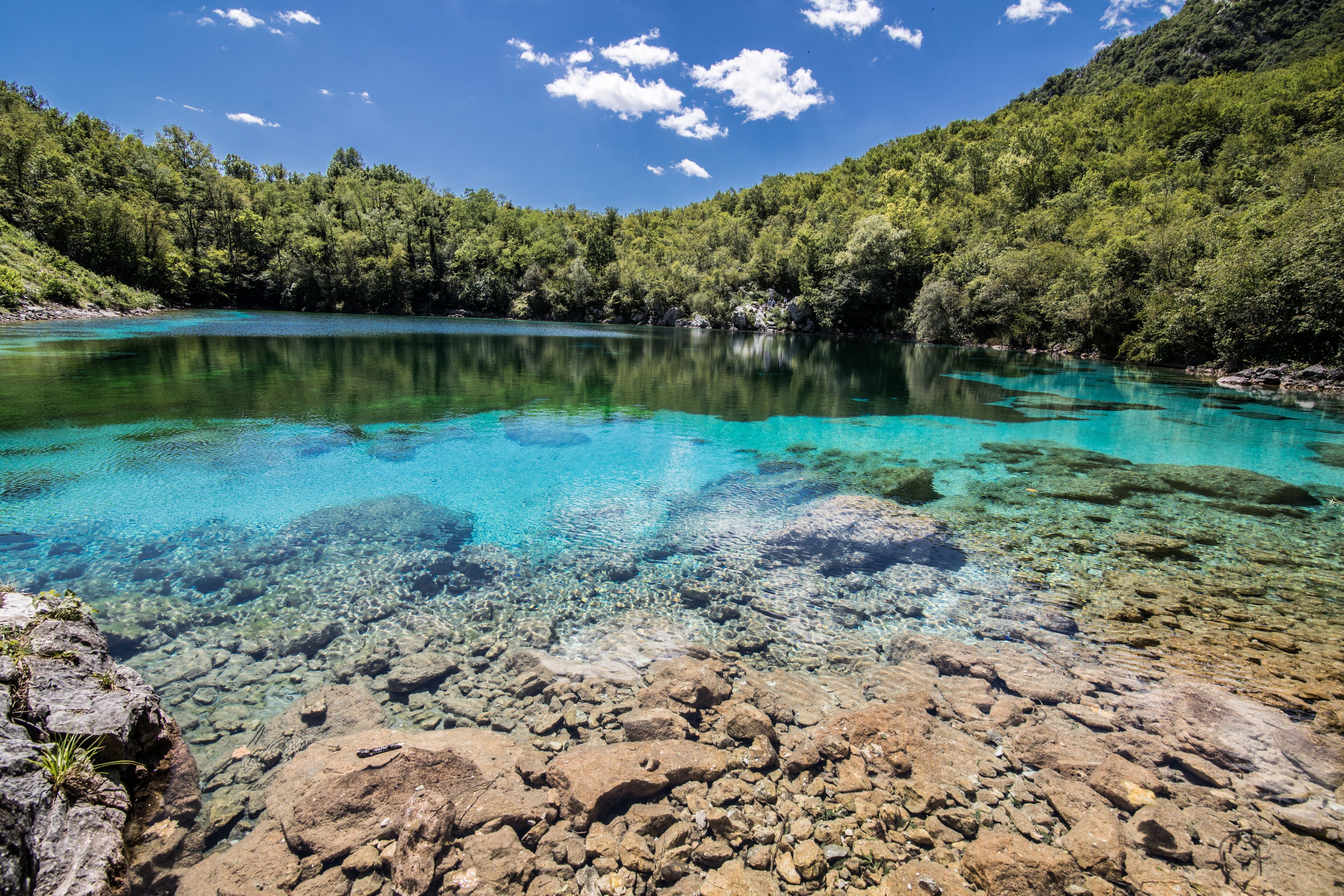 A clear turquoise lake surrounded by lush green hills.