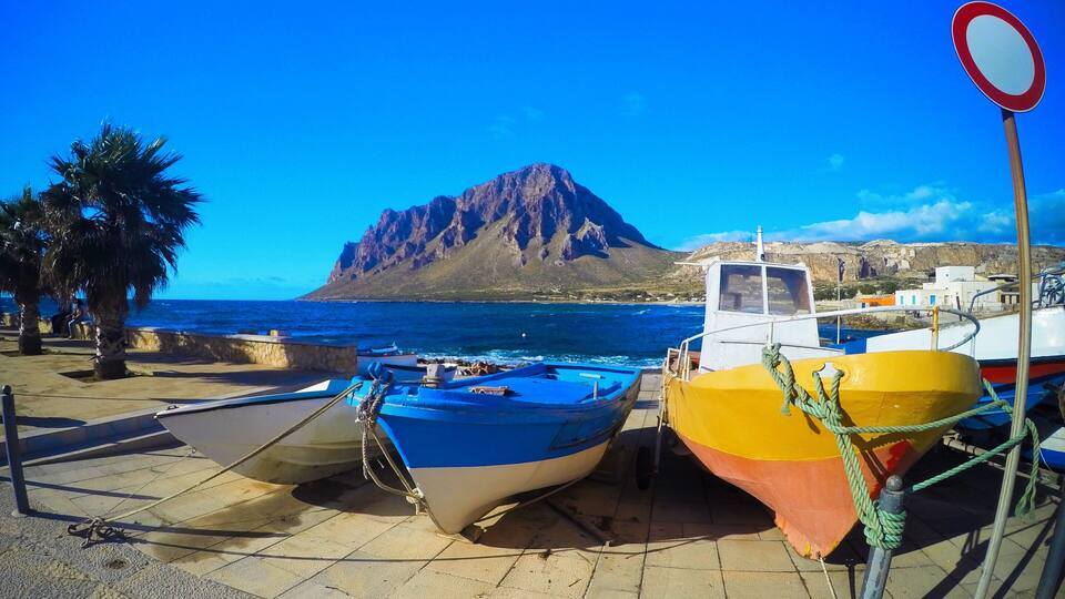 A coastal scene with boats docked, a mountain in the background, and a clear blue sky.