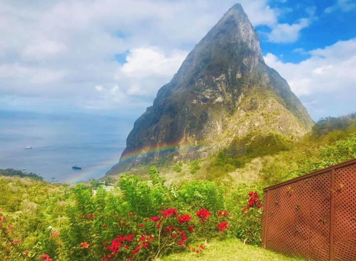 Una montaña con arcoíris, vegetación exuberante y vistas al mar.