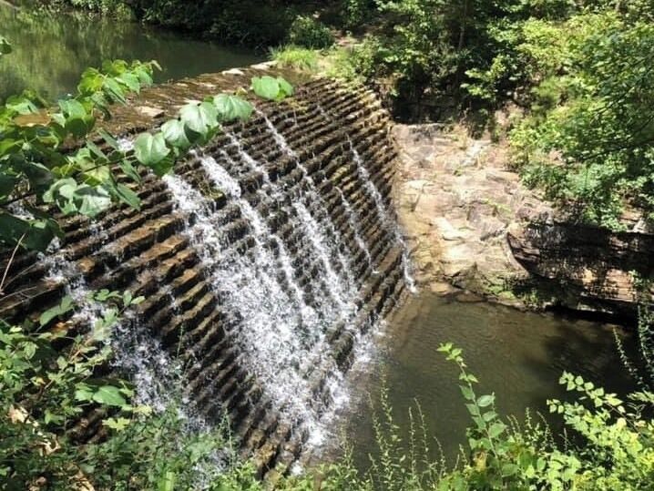 A waterfall cascading over a stone structure surrounded by lush greenery.