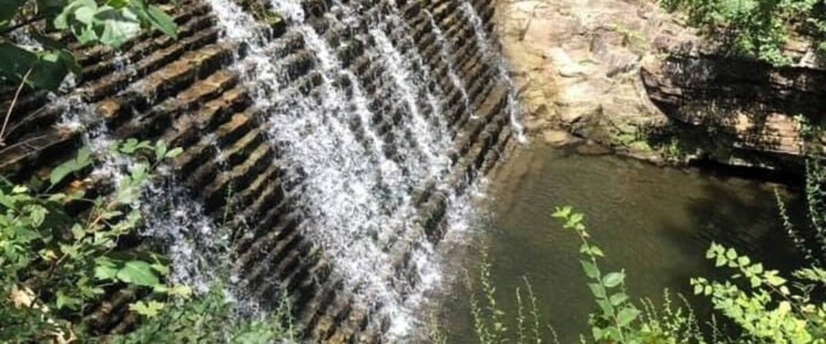 A waterfall cascading over a stone structure surrounded by lush greenery.
