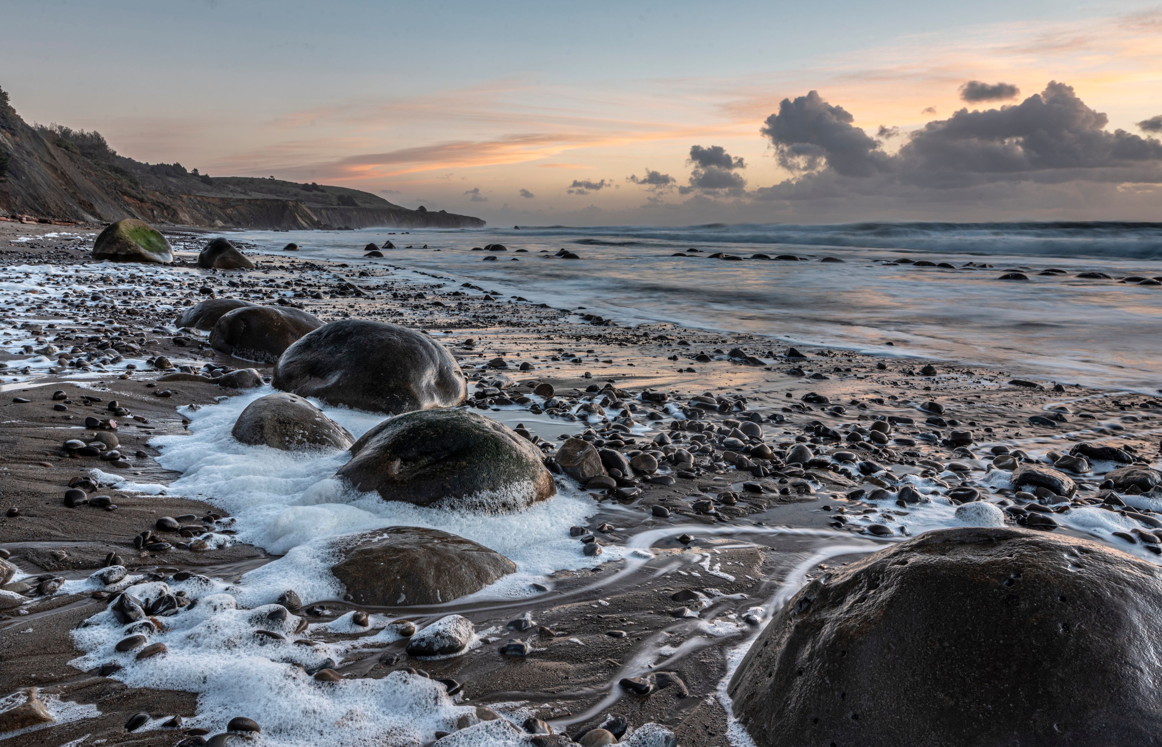 A rocky beach with large boulders and waves crashing onto the shore.