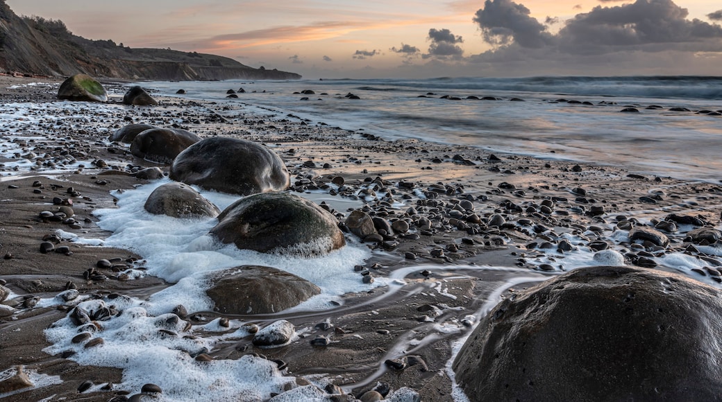 A rocky beach with large boulders and waves crashing onto the shore.