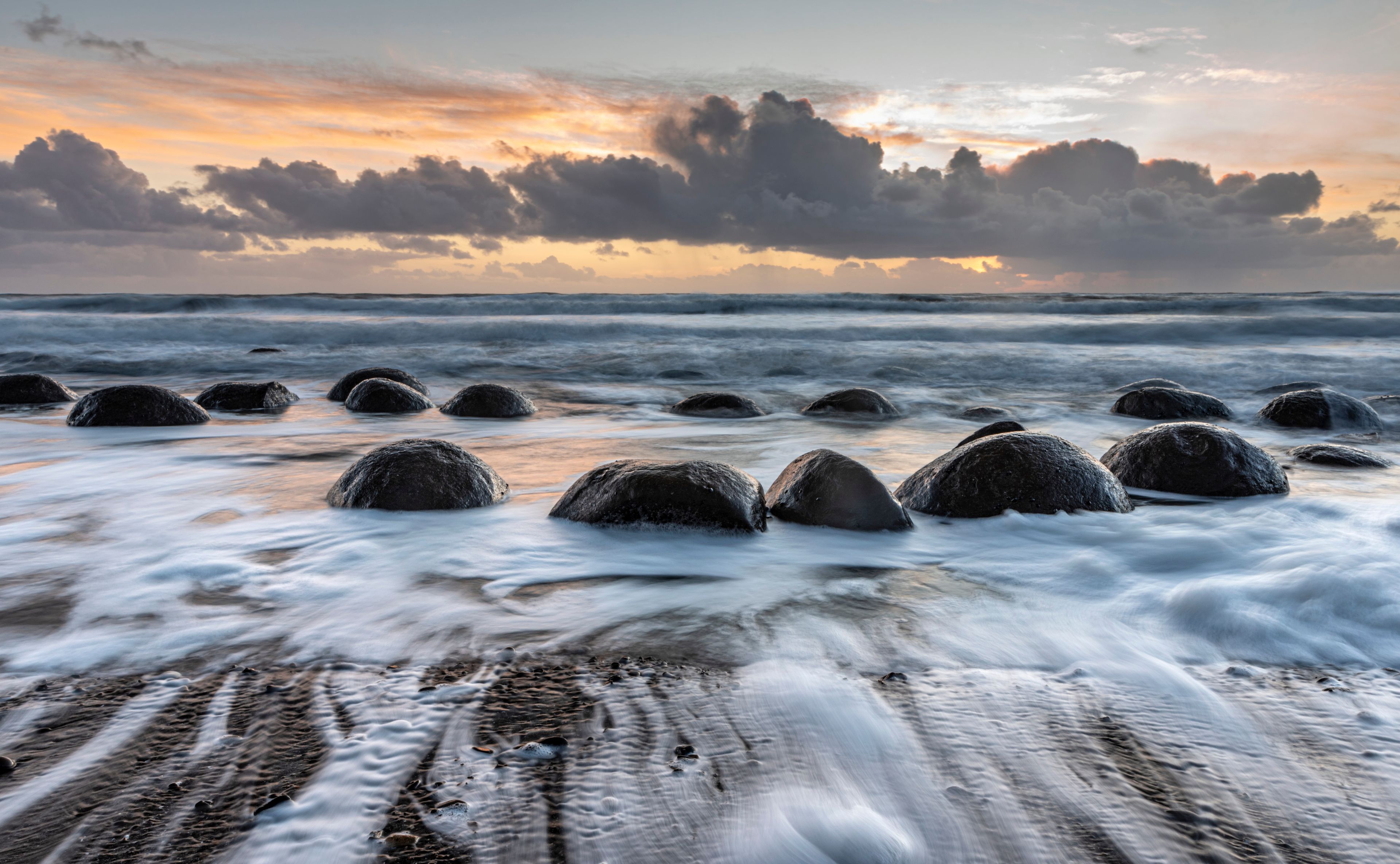 A beach with large rocks in the water and a sunset sky.