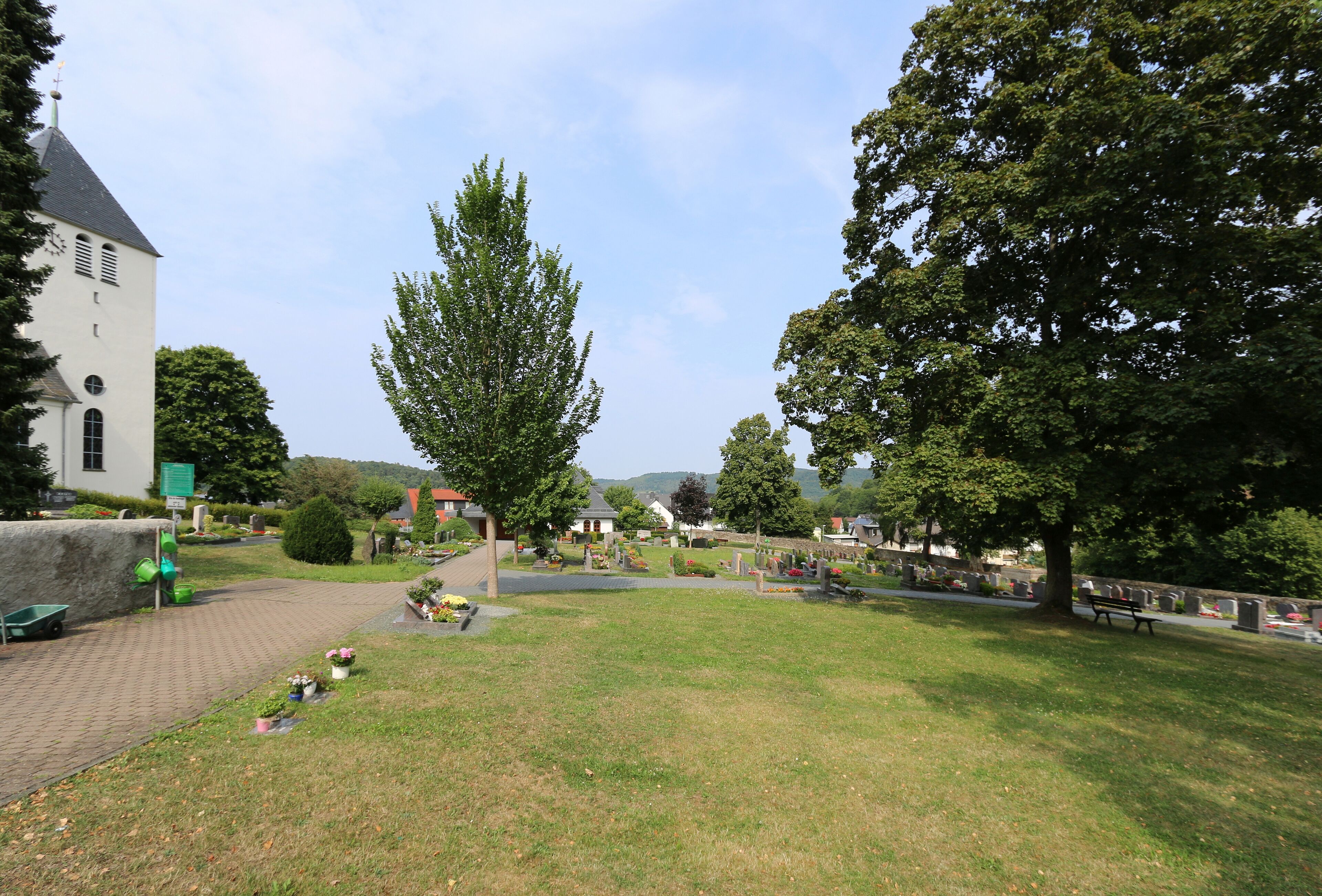 A cemetery with a church, trees, and a paved walkway.