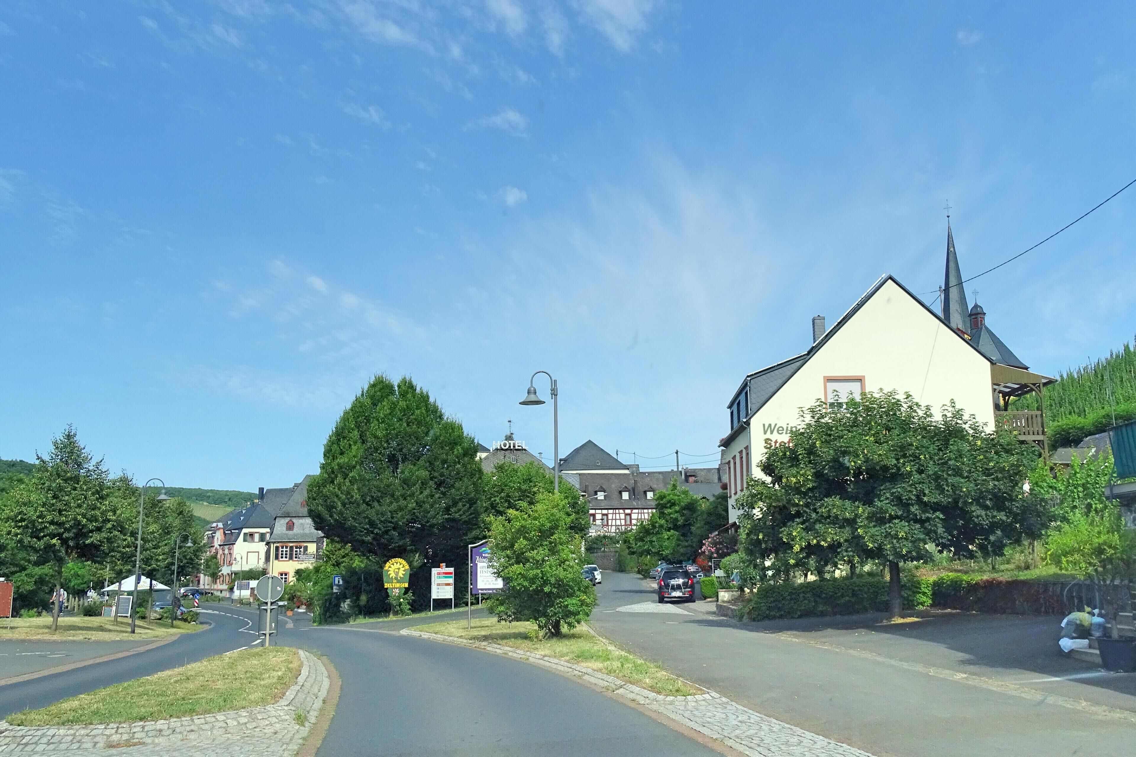 A sunny street in a small town with a church, a hotel, and a sign for a restaurant.