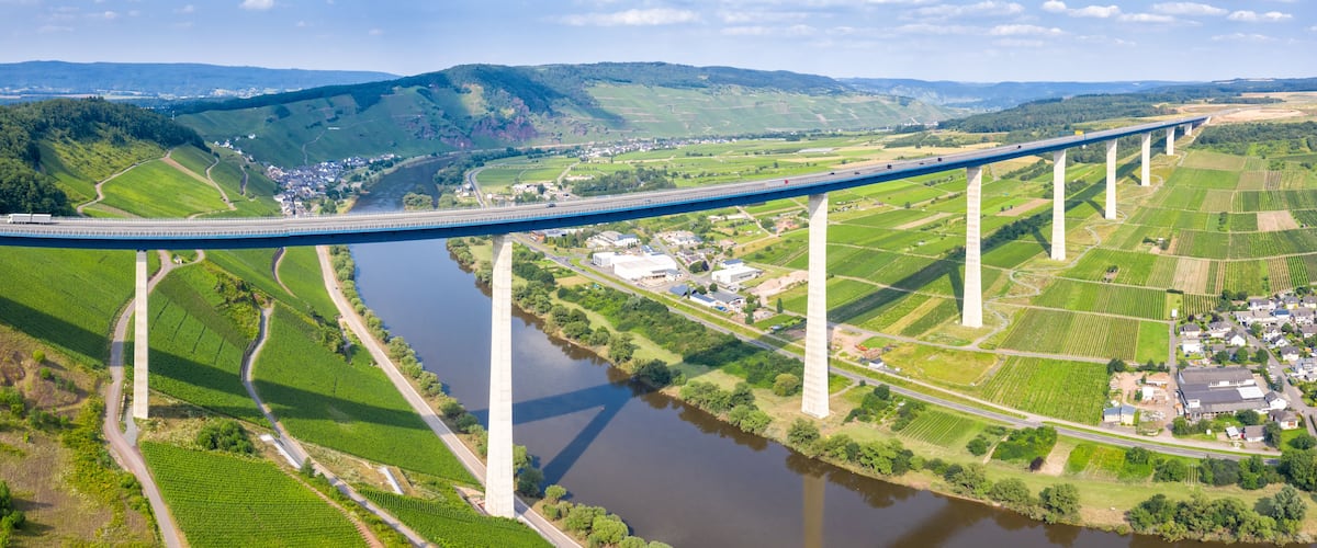 Un long pont enjambant une rivière, entouré de champs verdoyants et de petits bâtiments.