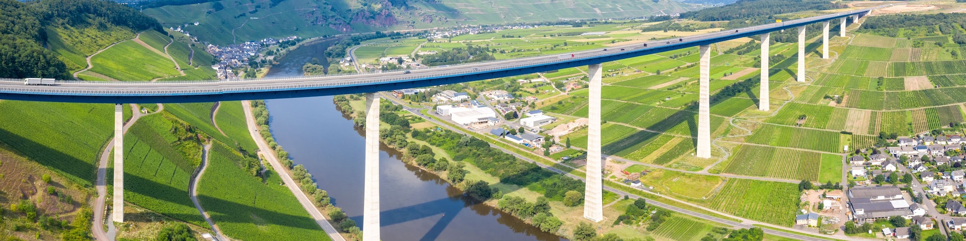 A long bridge spanning a river, surrounded by green fields and small buildings.