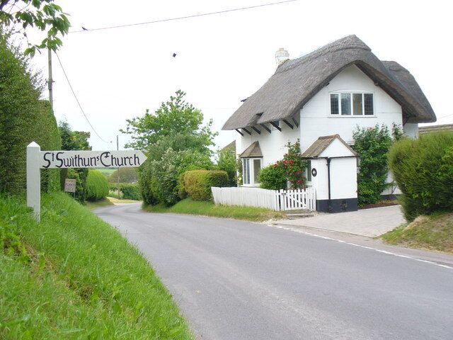 A white church with a thatched roof named St. Swythun's Church.