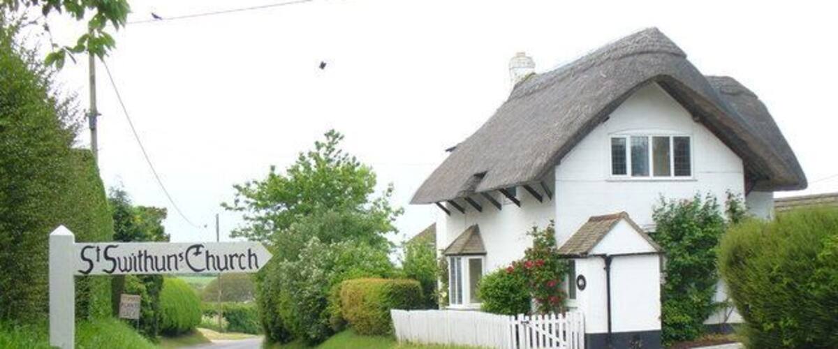 A white church with a thatched roof named St. Swythun's Church.