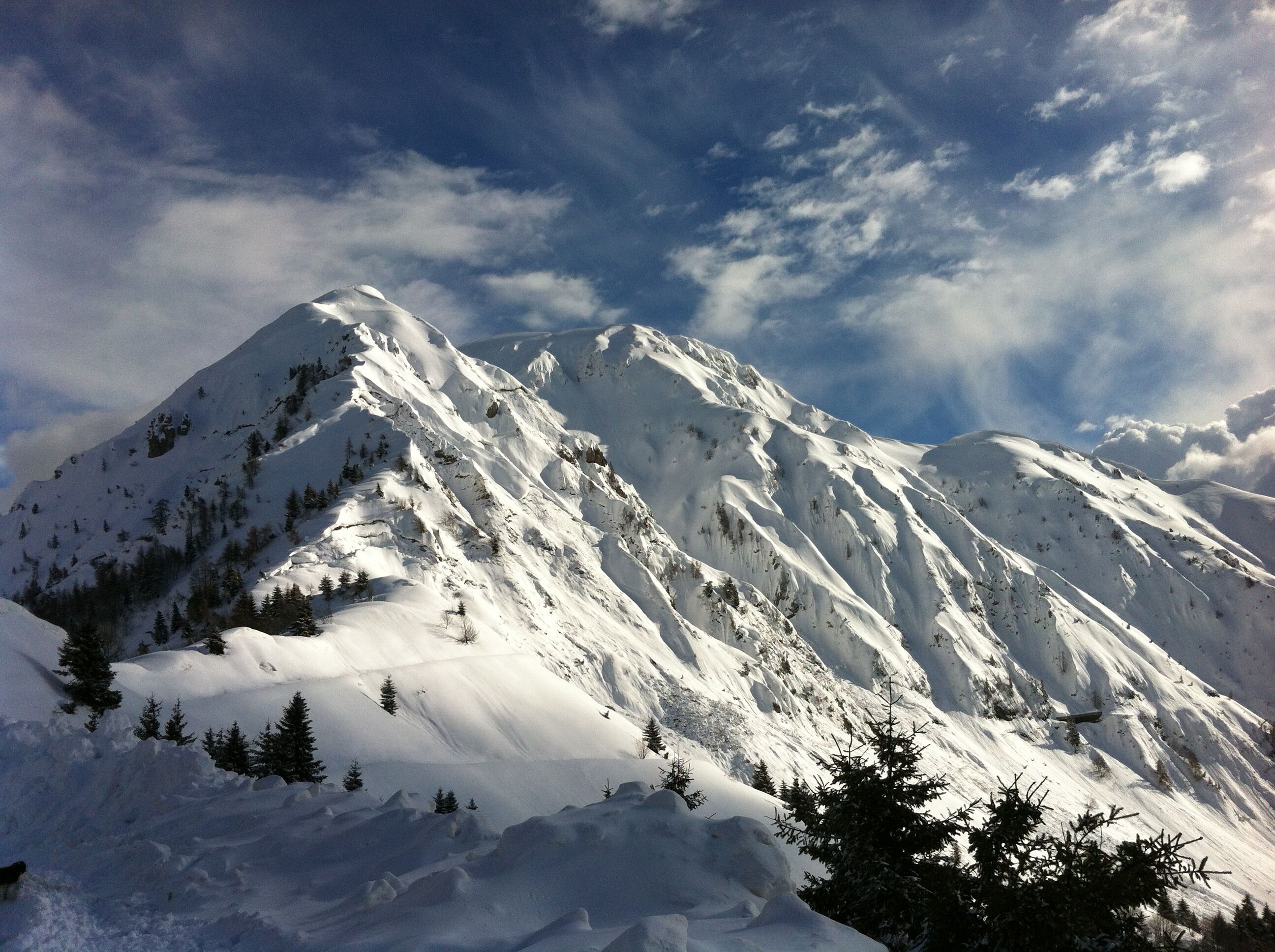 A snow-covered mountain peak with a clear sky and scattered clouds.