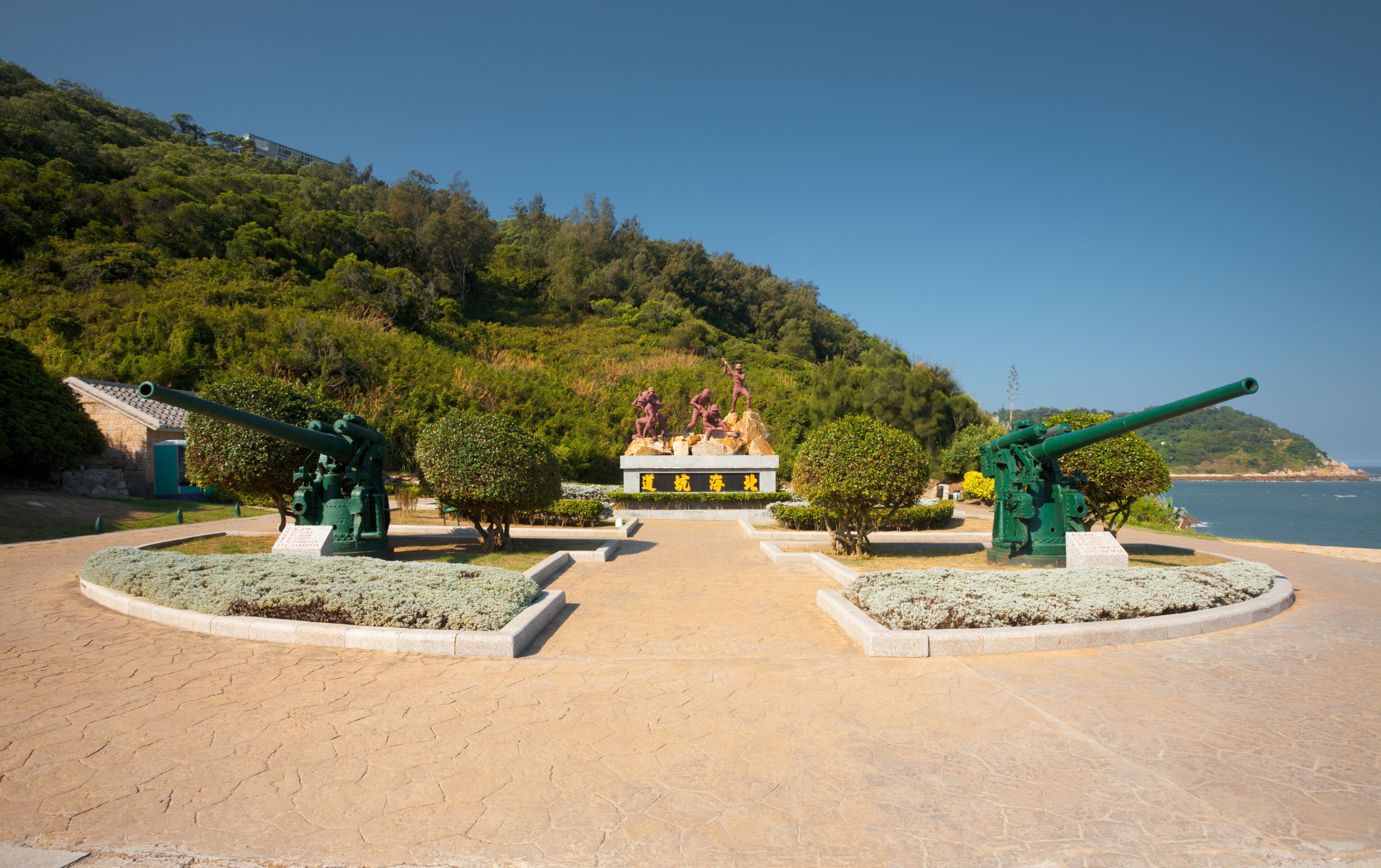 A coastal park with cannons, a monument, and a clear view of the sea.