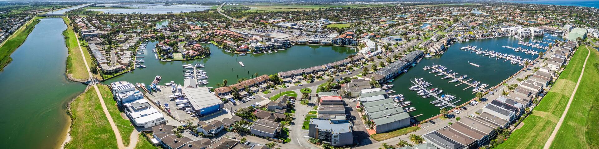 Aerial panorama of Patterson River and Patterson Lakes suburb on bright sunny day. Houses nested near water with moored boats nearby. Melbourne, Victoria, Australia