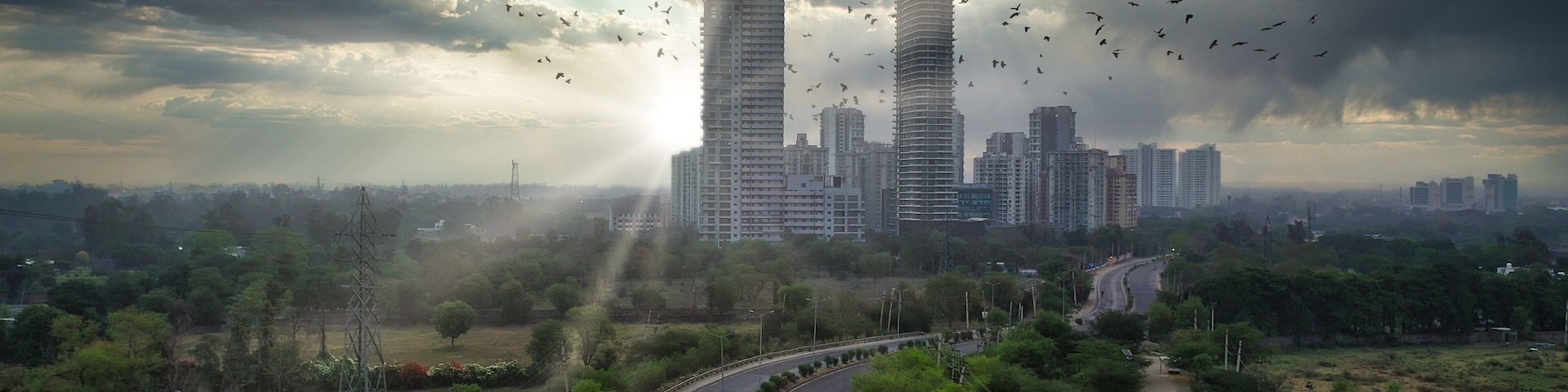 A cityscape with tall buildings, a curved road, and a cloudy sky.