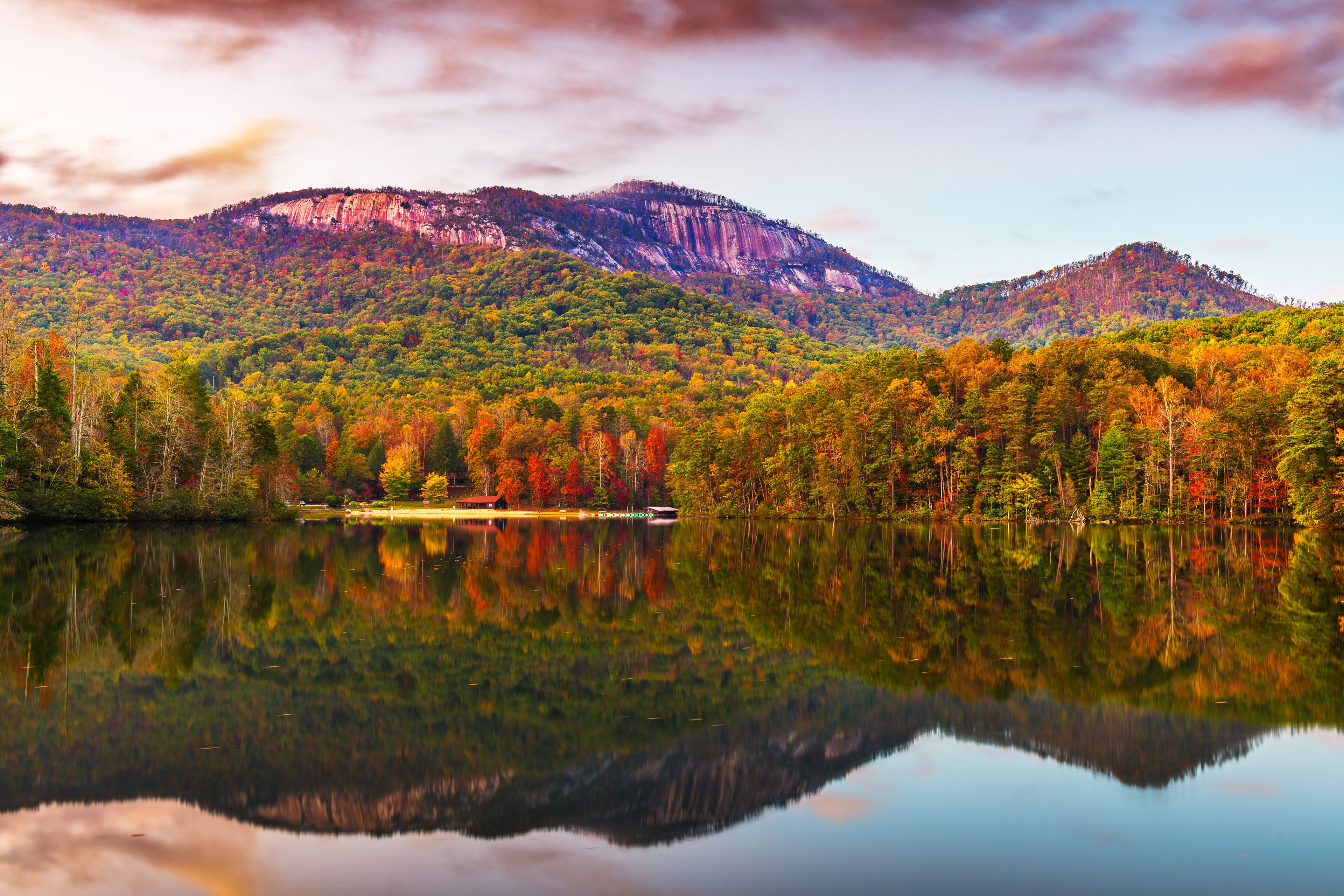 A calm lake reflecting colorful autumn trees and a mountain range.