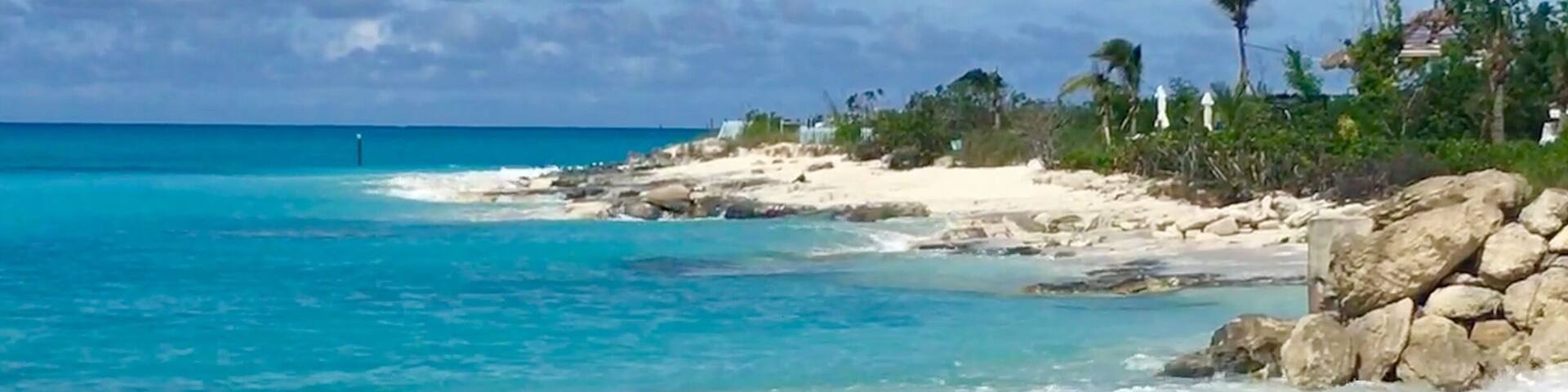 A beach with turquoise water, white sand, and rocky outcrops.