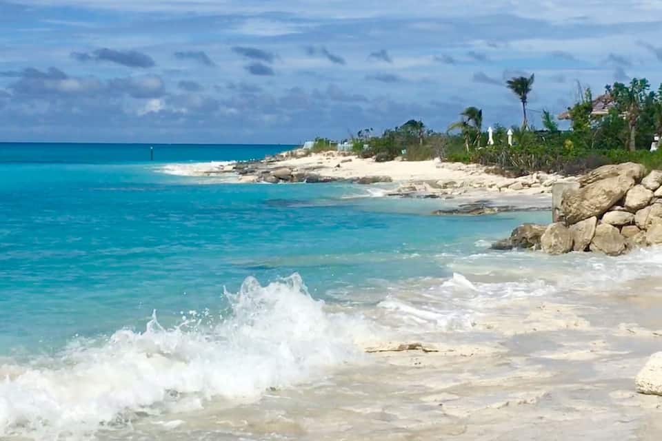 A beach with turquoise water, white sand, and rocky outcrops.