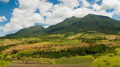 A mountainous landscape with lush green fields and a clear blue sky with clouds.
