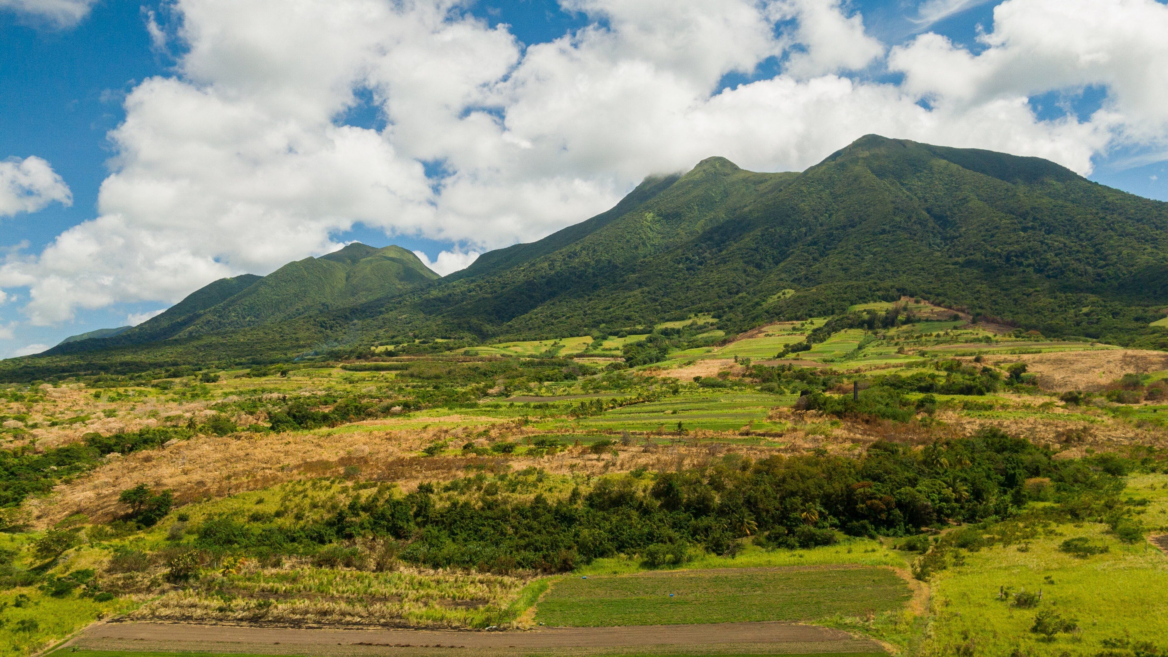 A mountainous landscape with lush green fields and a clear blue sky with clouds.