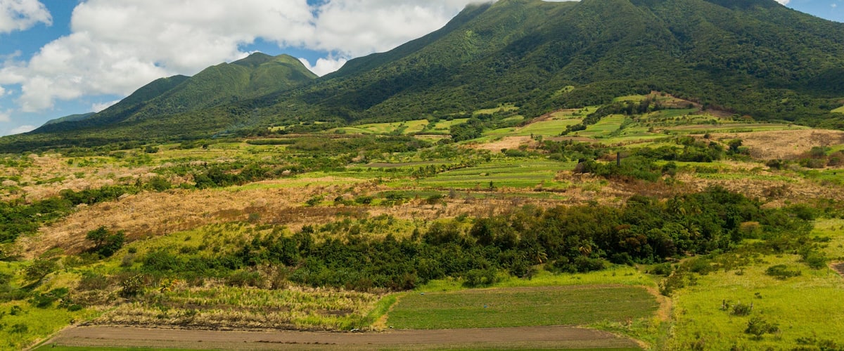 A mountainous landscape with lush green fields and a clear blue sky with clouds.