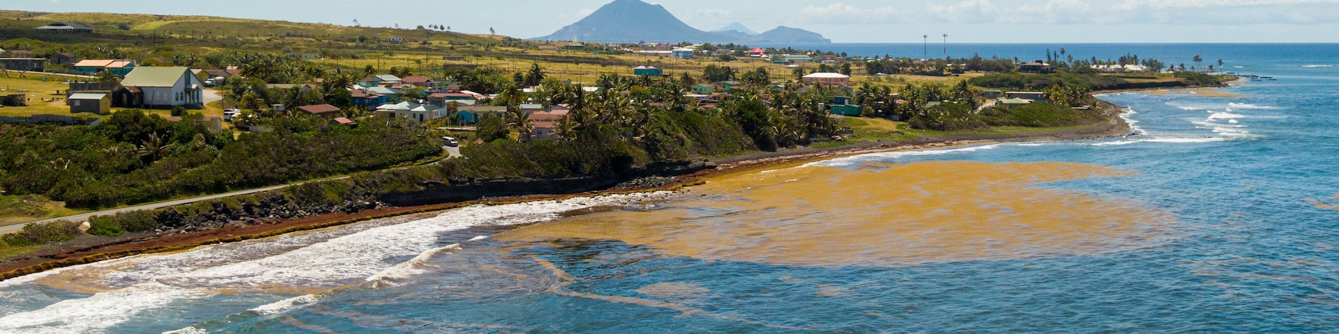 Un pueblo costero con casas, una playa y una montaña al fondo.