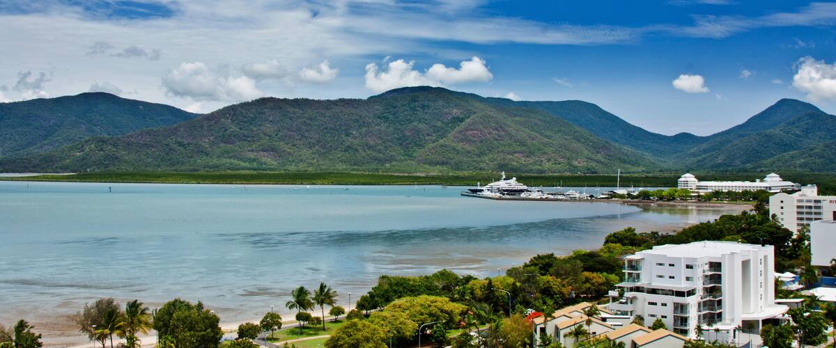 A coastal city with a large body of water, mountains in the background, and a cruise ship docked near the shore.