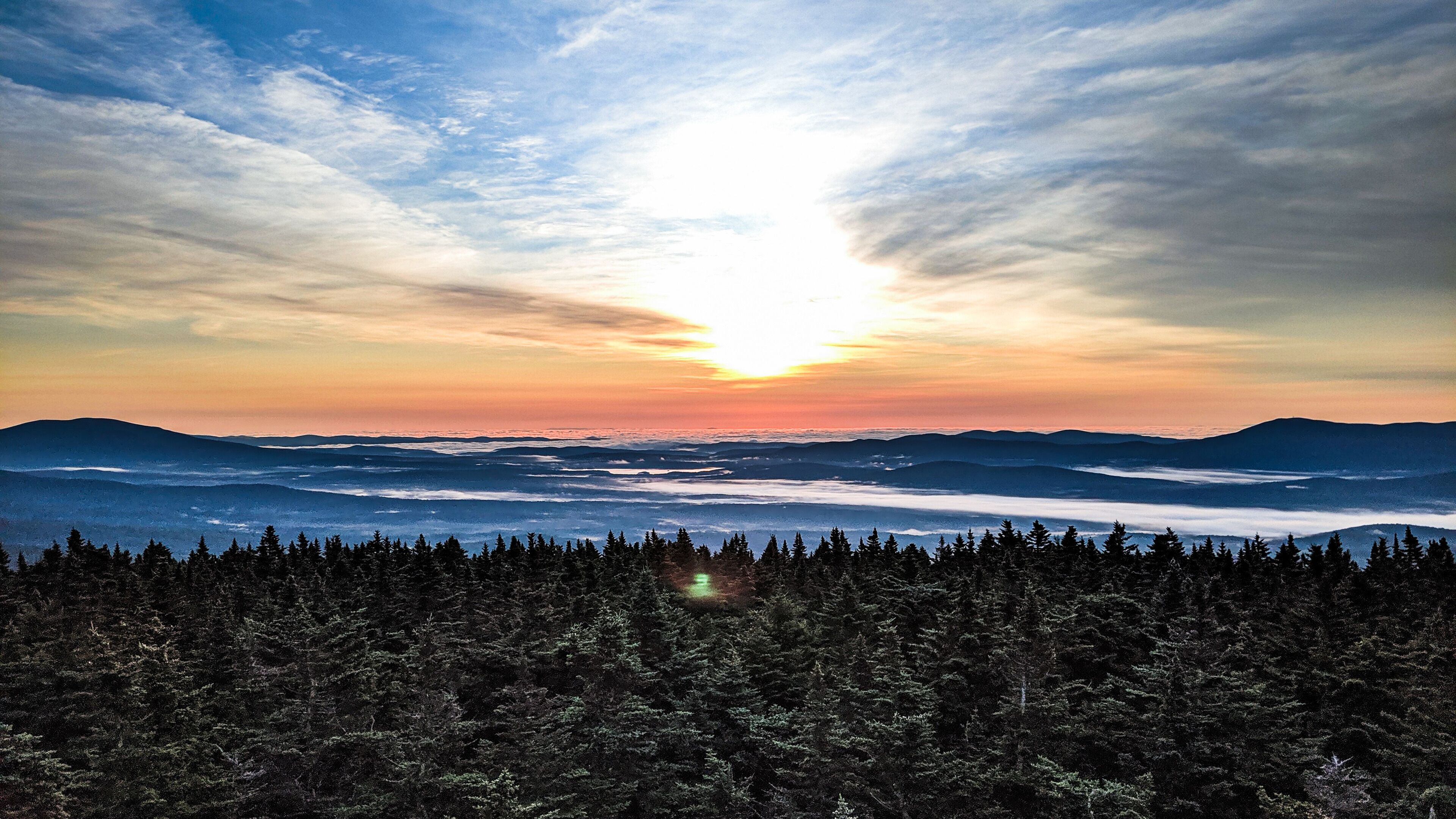 A forested mountain range with a sunset over a valley.