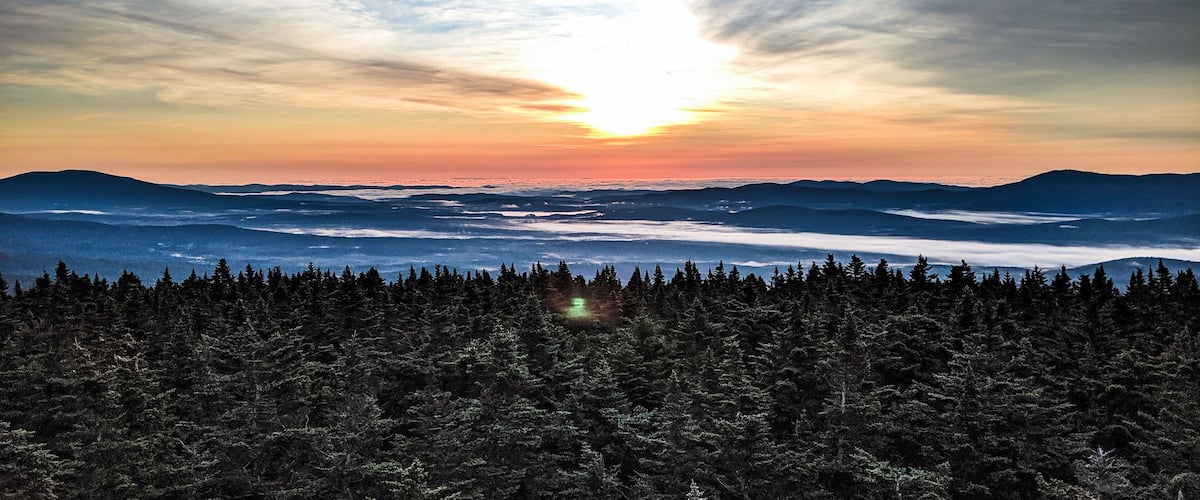A forested mountain range with a sunset over a valley.