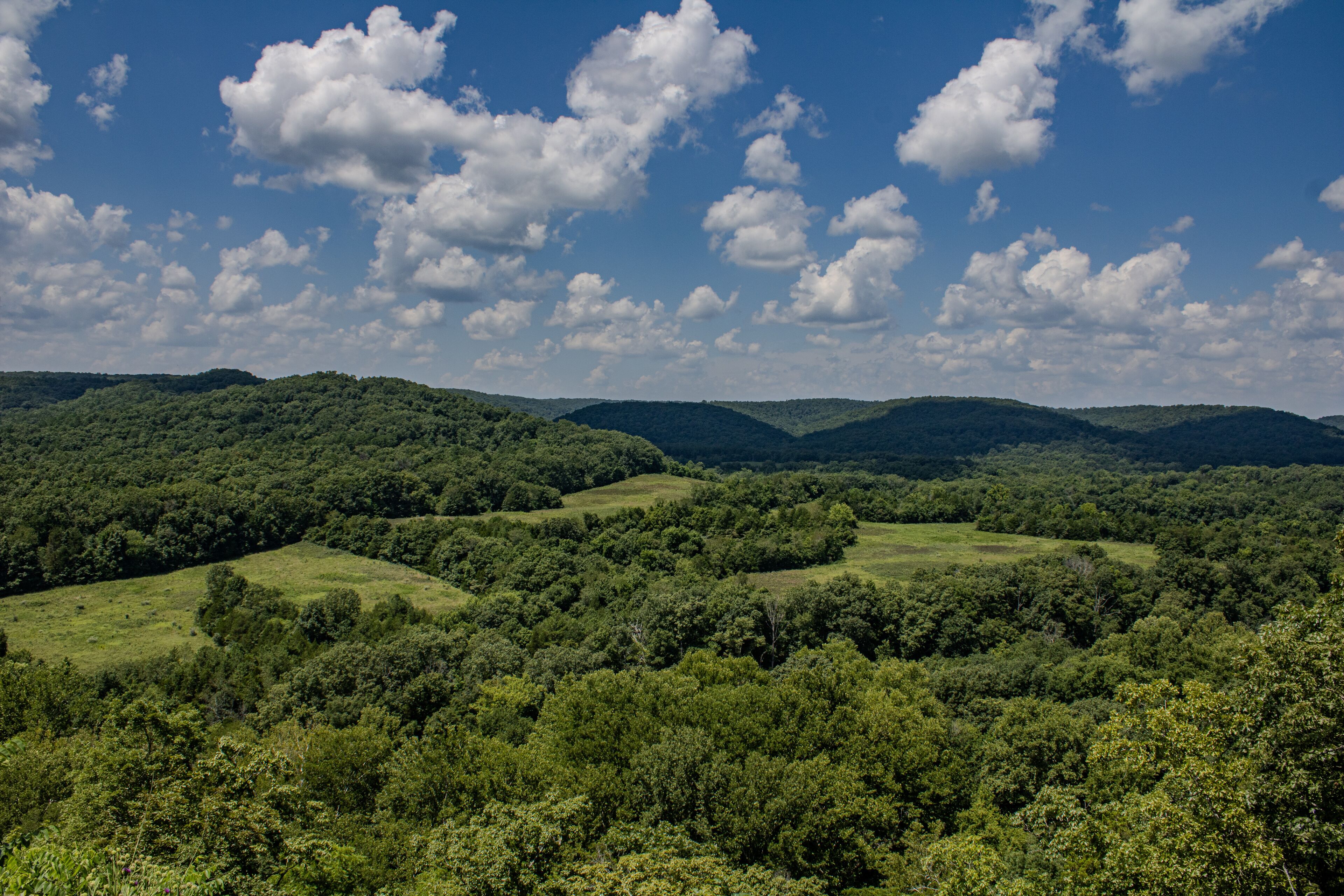 A lush green valley with rolling hills and a clear blue sky with scattered clouds.