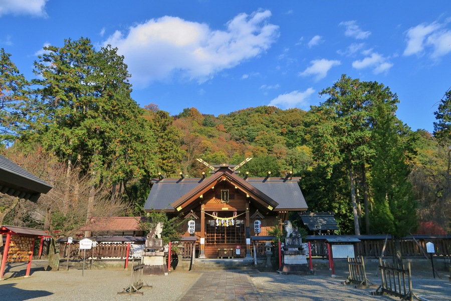 A traditional Japanese building with a sloped roof, surrounded by trees and a clear blue sky.