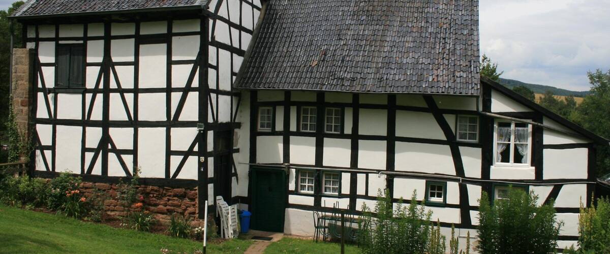 A traditional half-timbered house with a sloped roof and a stone wall foundation.