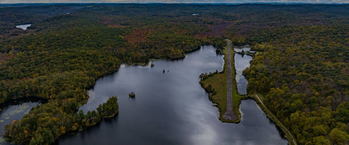 Aerial view of the countryside in Stormville, NY on a cloudy day during the colorful autumn season with a lake in view.