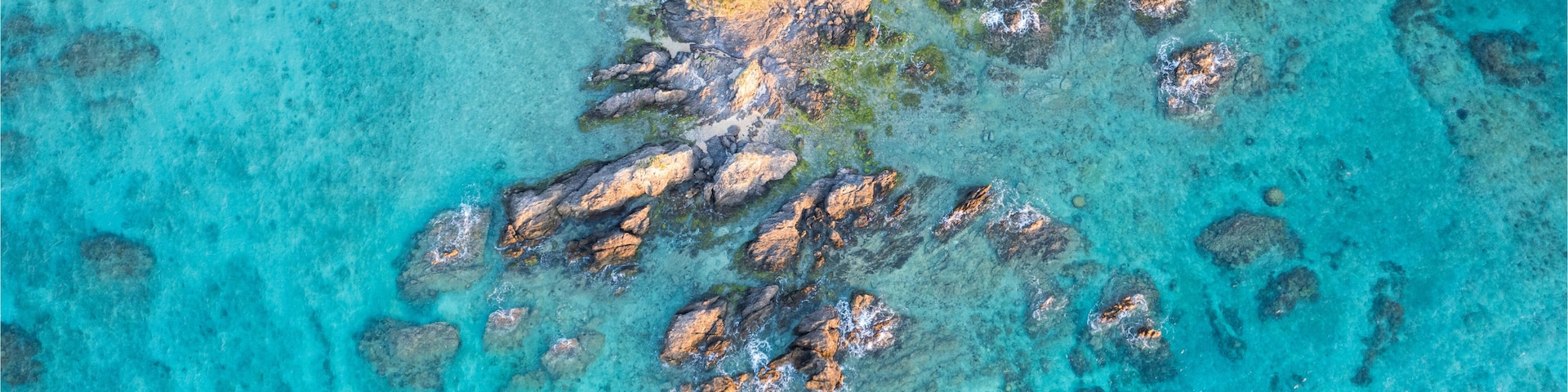 Mar turquesa com afloramentos rochosos e uma praia de areia.