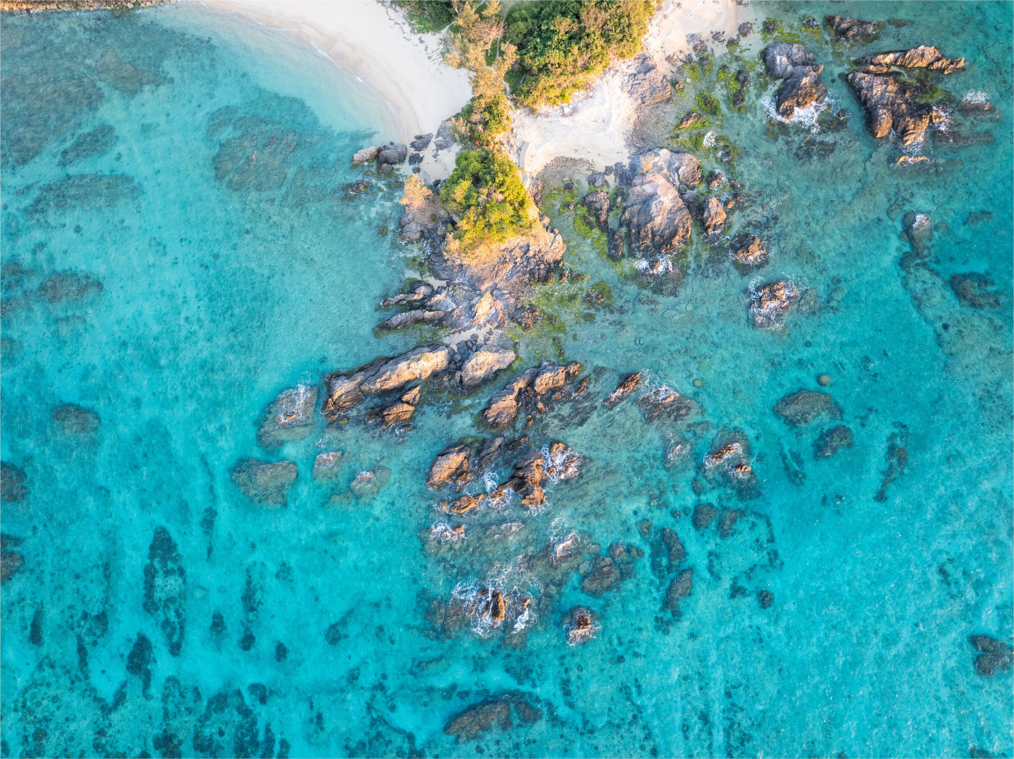 A turquoise sea with rocky outcrops and a sandy beach.