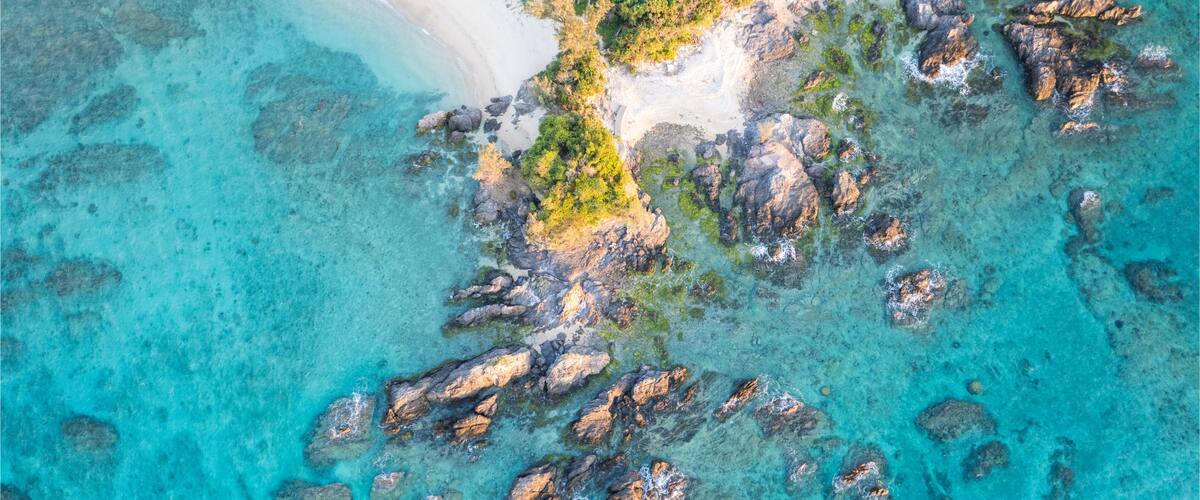 A turquoise sea with rocky outcrops and a sandy beach.