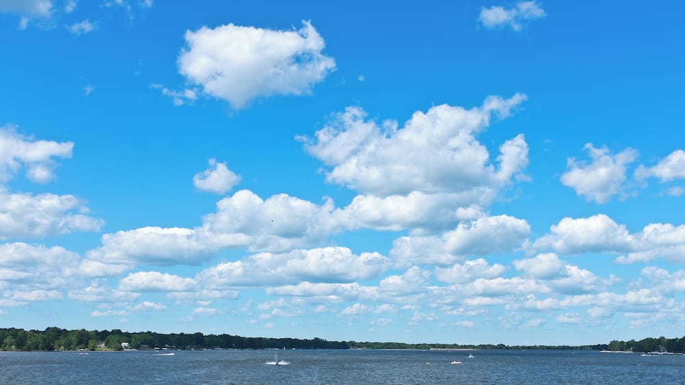 A body of water with boats, a clear sky, and scattered clouds.