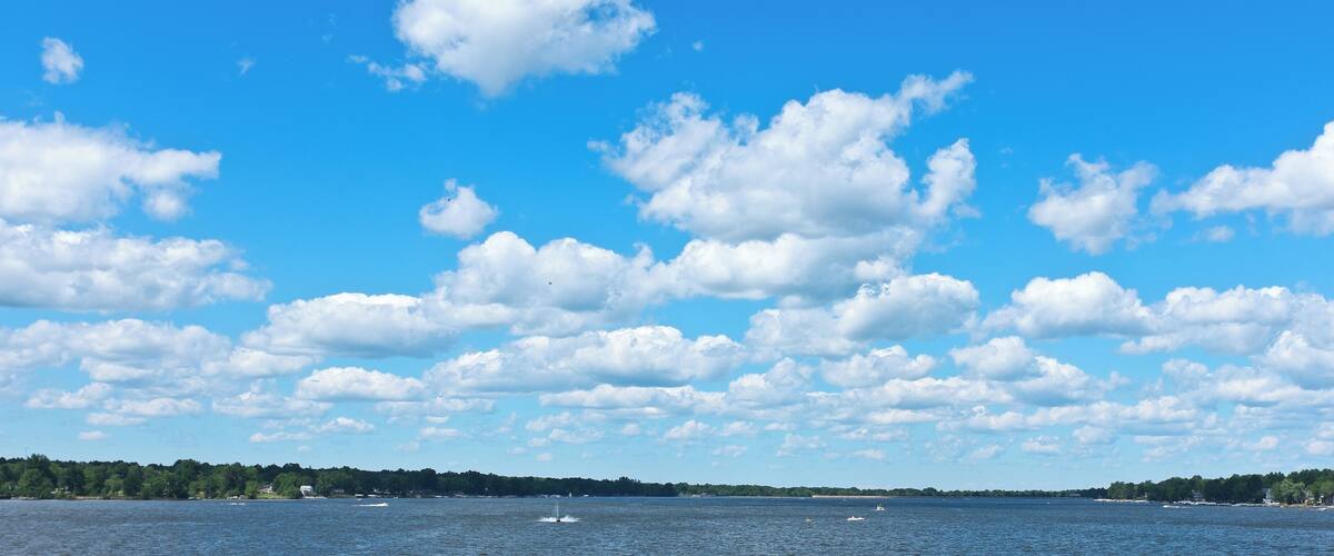 A body of water with boats, a clear sky, and scattered clouds.
