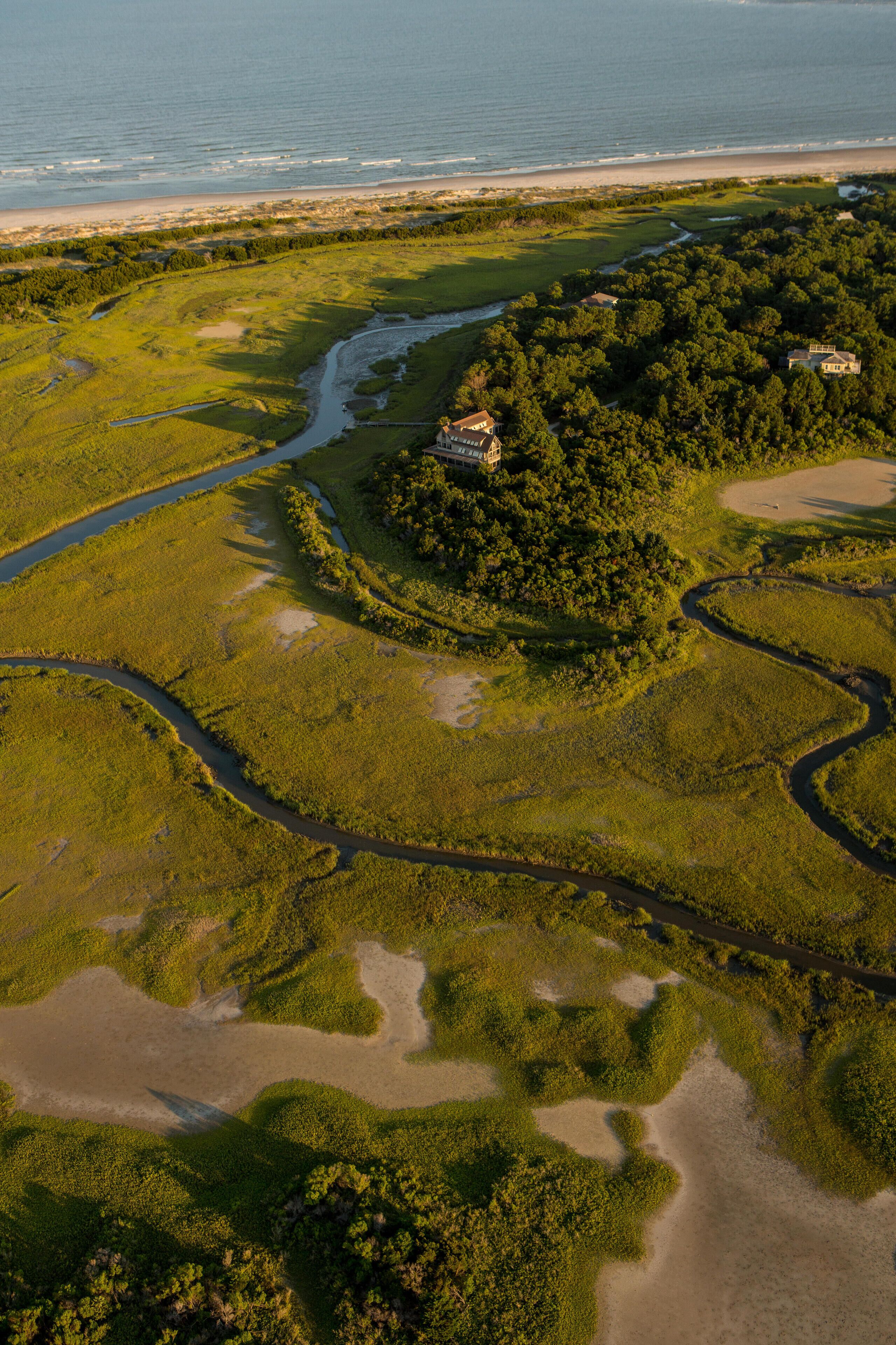 An aerial view of a coastal landscape with a river, dense forest, and a beach.