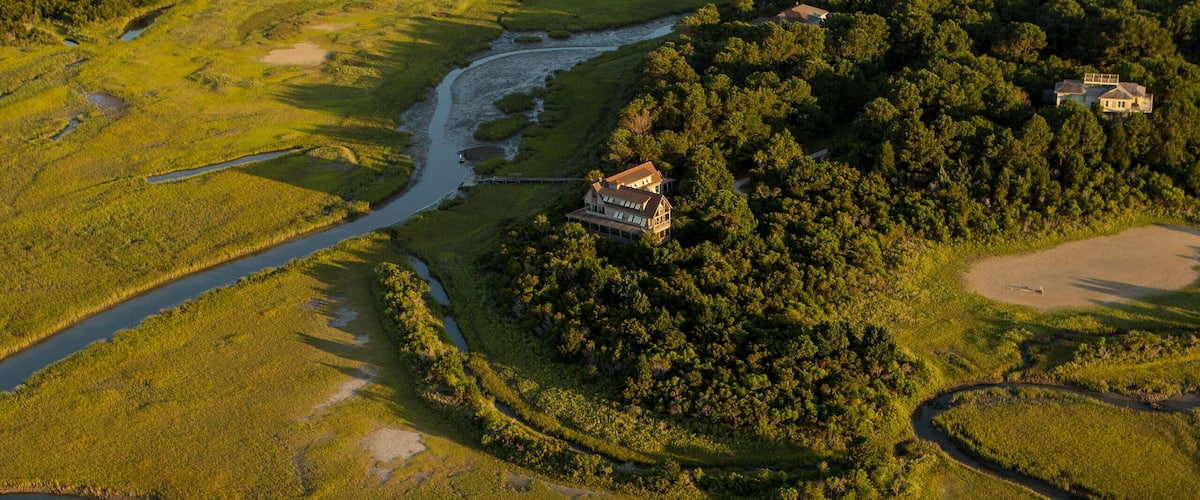 An aerial view of a coastal landscape with a river, dense forest, and a beach.