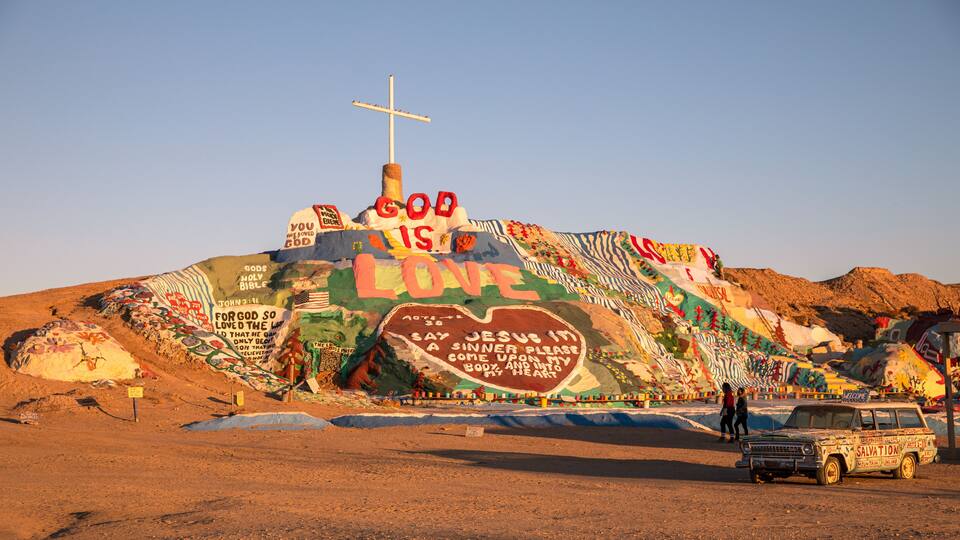 A large, colorful mural on a hill with a cross at the top.