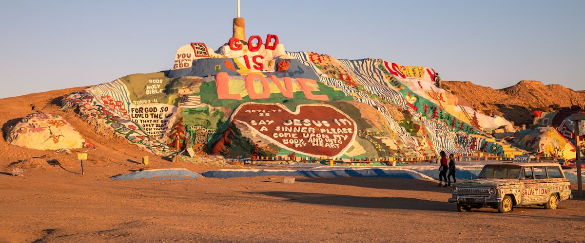 A large, colorful mural on a hill with a cross at the top.