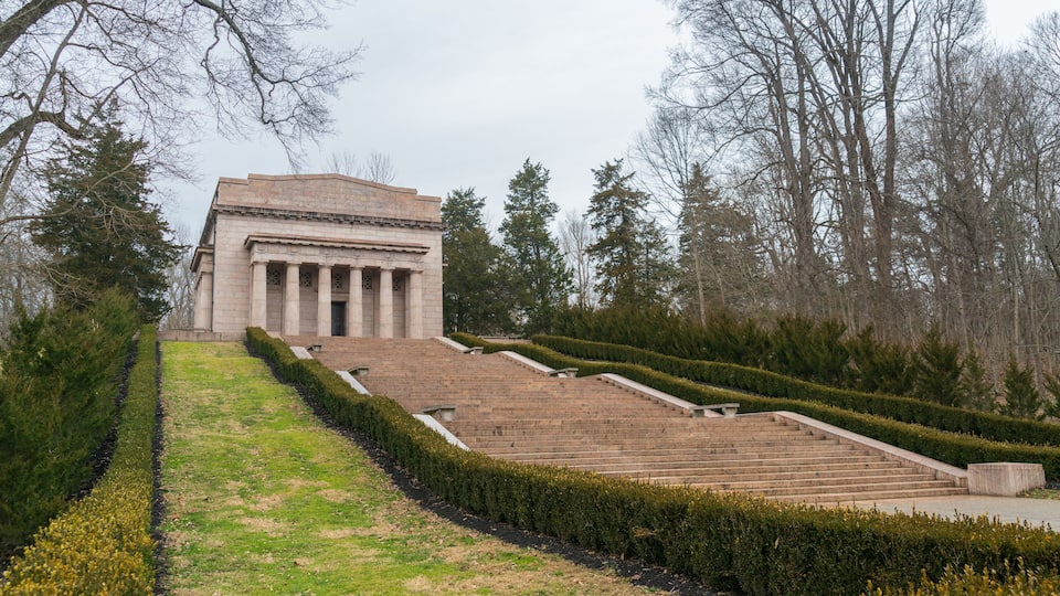 A neoclassical building with columns, surrounded by a landscaped garden with a staircase leading up to it.