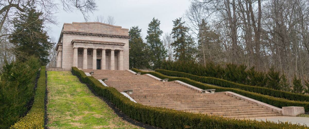 A neoclassical building with columns, surrounded by a landscaped garden with a staircase leading up to it.