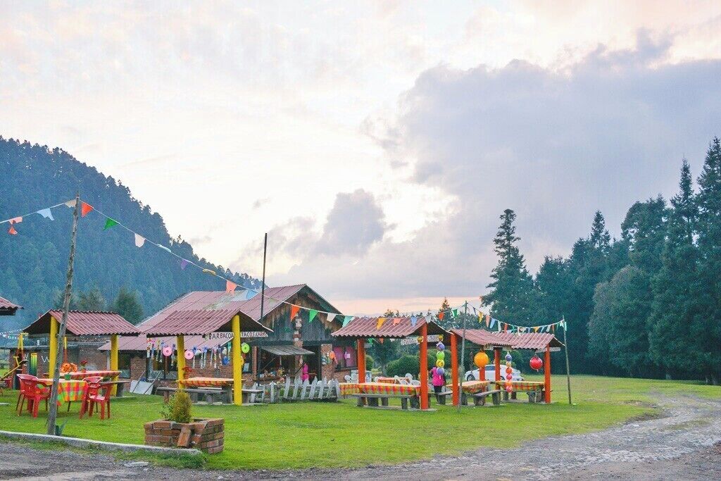 A rustic outdoor dining area with wooden structures and colorful decorations against a mountainous backdrop.