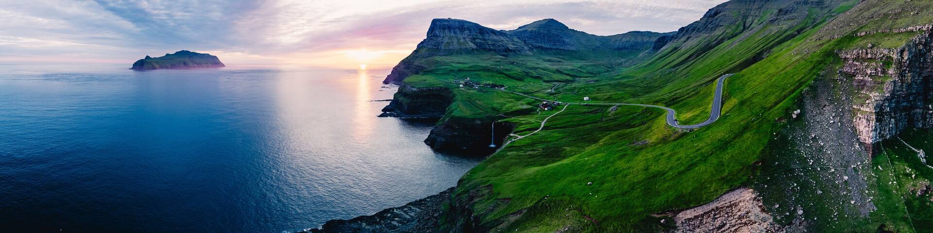 Golden light cascades over the dramatic cliffs surrounding Mulafossur waterfall, with Gasadalur village nestled below. Faroe Islands